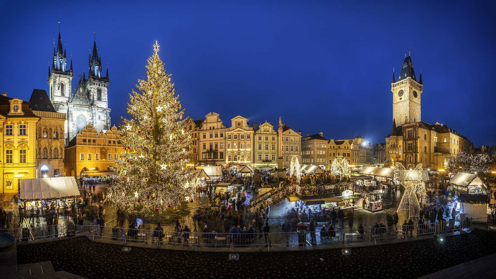 Et smukt oplyst julemarked på et bytorv med et stort strålende juletræ om aftenen.